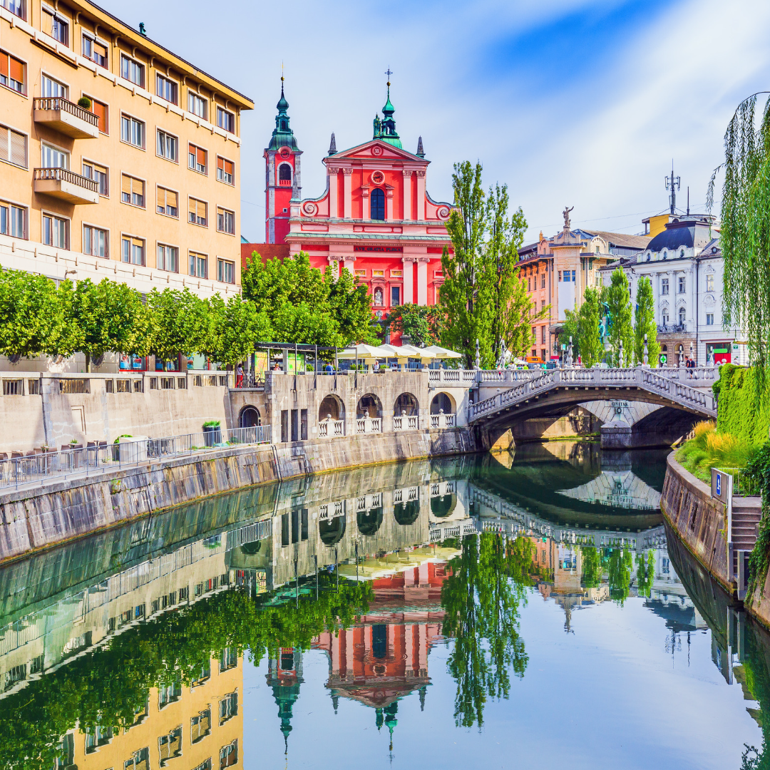A scenic landscape of Slovenia featuring historic architecture, lush green hills, and a tranquil river—a picturesque destination for travel and tourism.